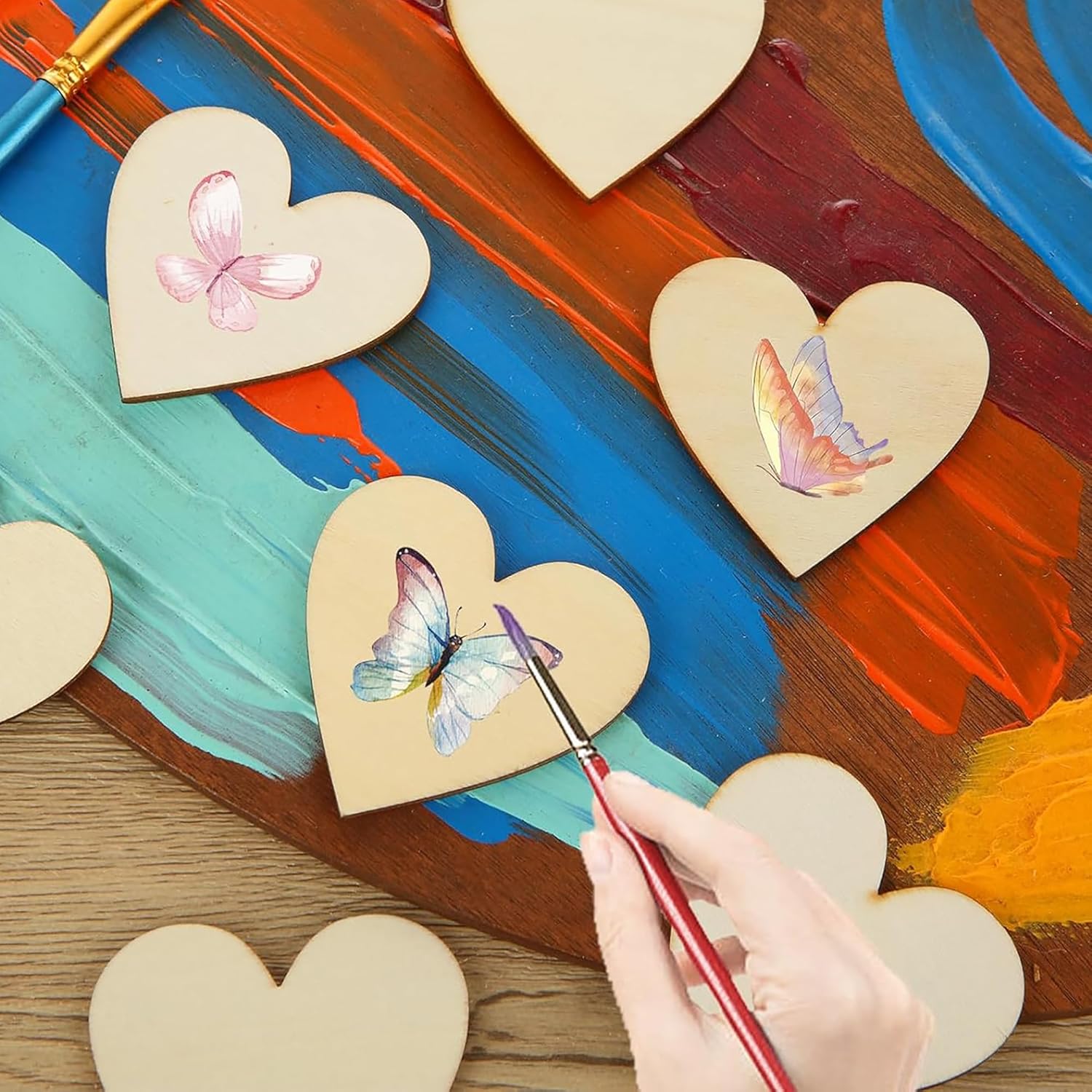 Heart-shaped wooden pieces with butterfly designs being painted on a colorful background