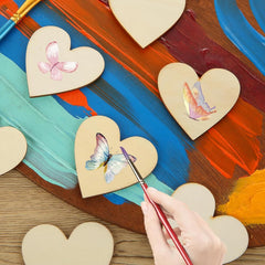 Heart-shaped wooden pieces with butterfly designs being painted on a colorful background