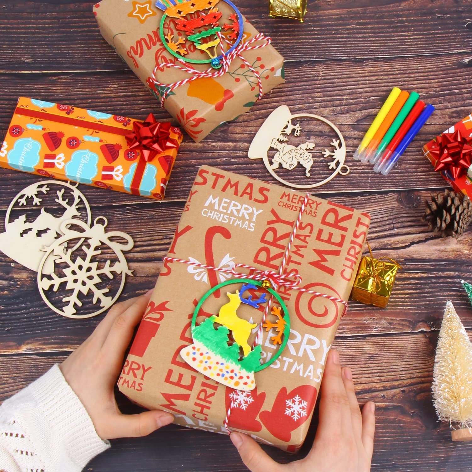 Hand holding a Christmas-themed gift wrapped in brown paper with decorative elements on a wooden surface.