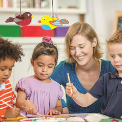 Teacher and students engaged in a craft activity with colorful birds hanging above.