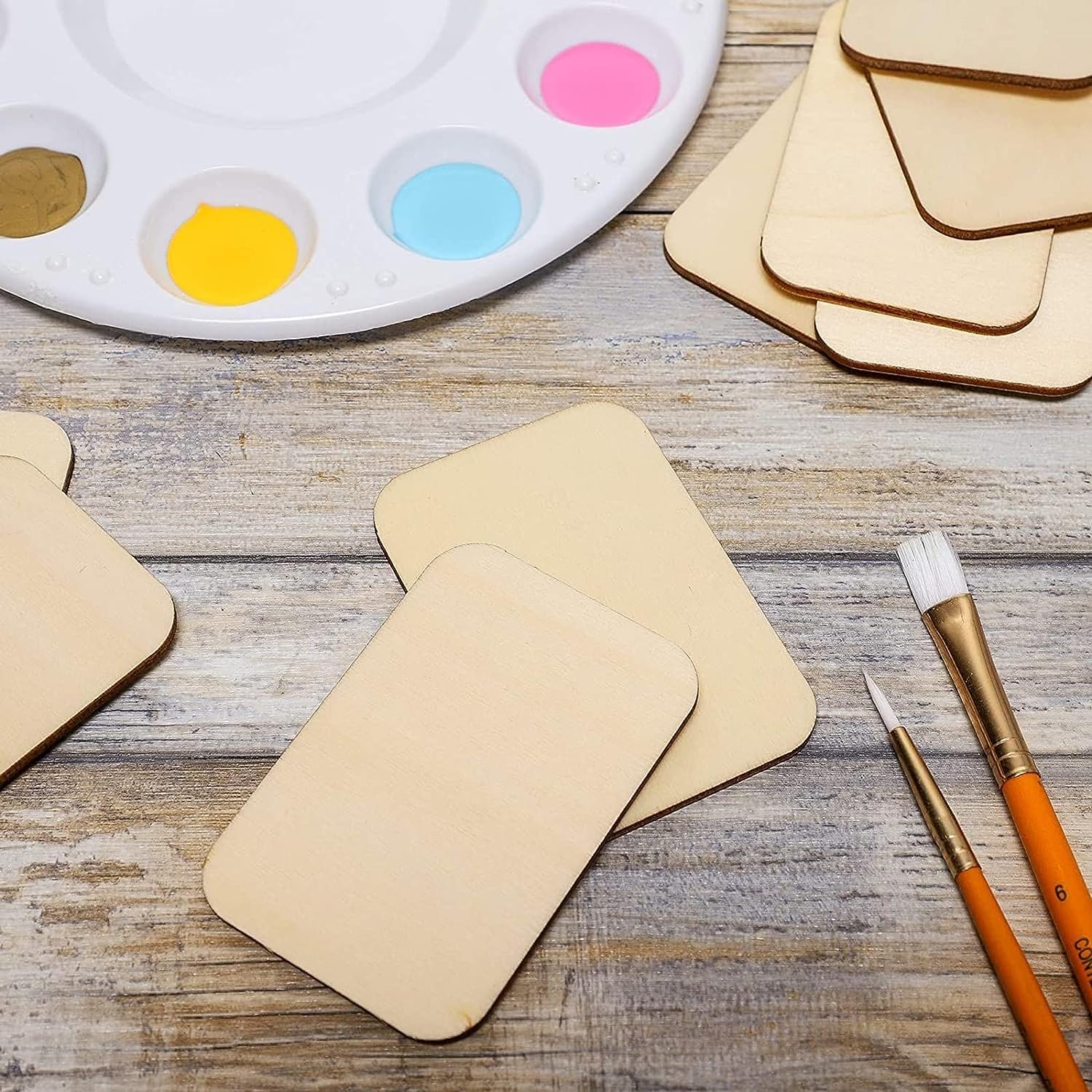 Beige cardboard shapes, paintbrushes, and a color palette on a wooden surface