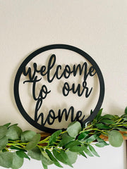 Decorative wall art with 'welcome to our home' text and greenery on a neutral background