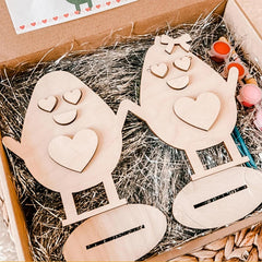 Wooden house-shaped cutouts with heart details on a straw-lined box.
