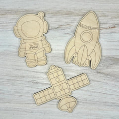 Wooden cutouts of an astronaut, rocket, and airplane on a wooden surface