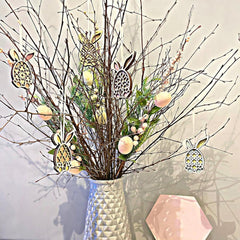 Decorative arrangement with branches, Easter eggs, and bunny ornaments in a vase on a light background.