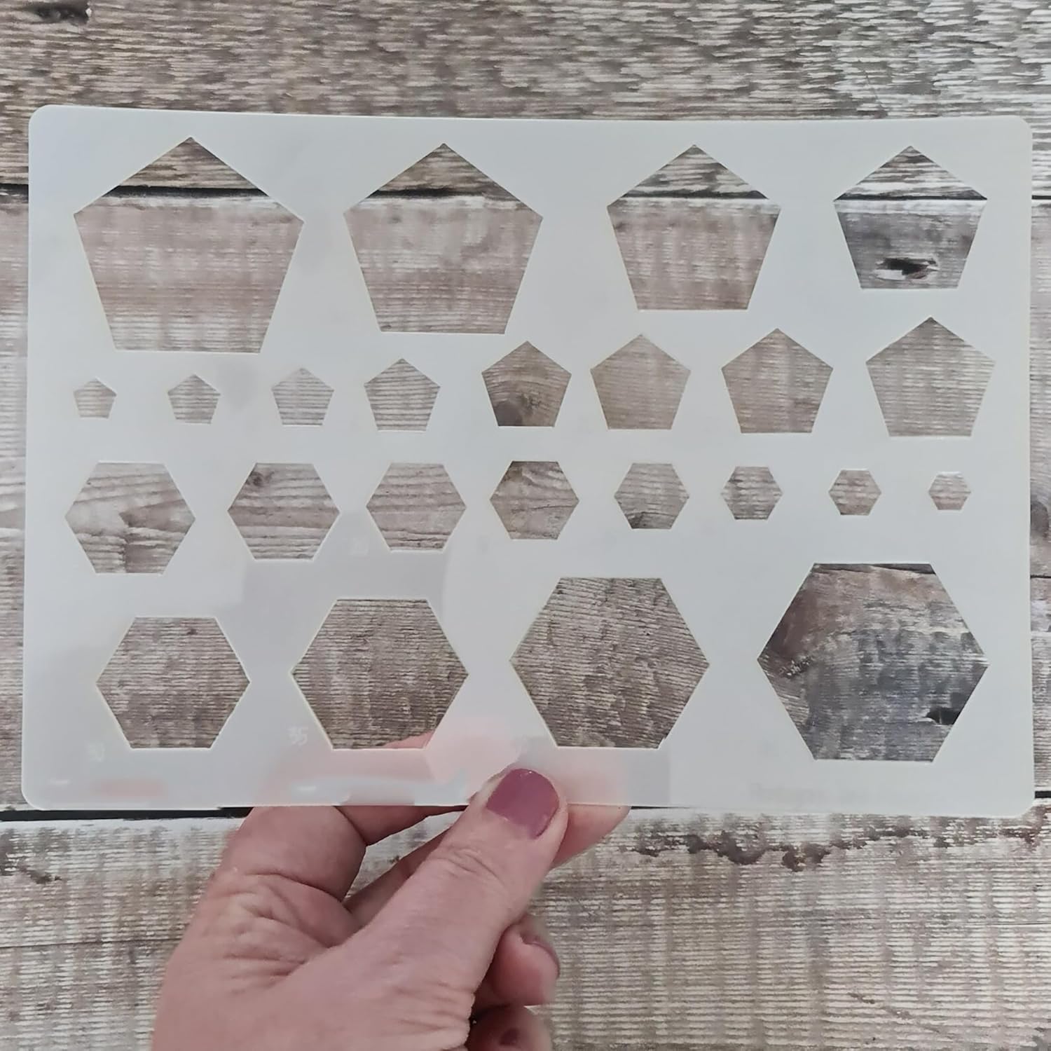Hand holding a geometric patterned stencil against a wooden background