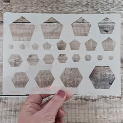 Hand holding a geometric patterned stencil against a wooden background