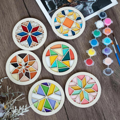 Set of colorful geometric coasters on a wooden surface with paint bottles and brushes.