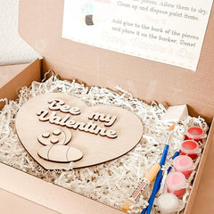 Wooden heart-shaped plaque with 'Bee my Valentine' text, paint supplies, and instructions in a box.