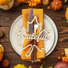 Thanksgiving table setting with 'Grateful' decoration, knife, fork, and yellow napkin on a wooden background.