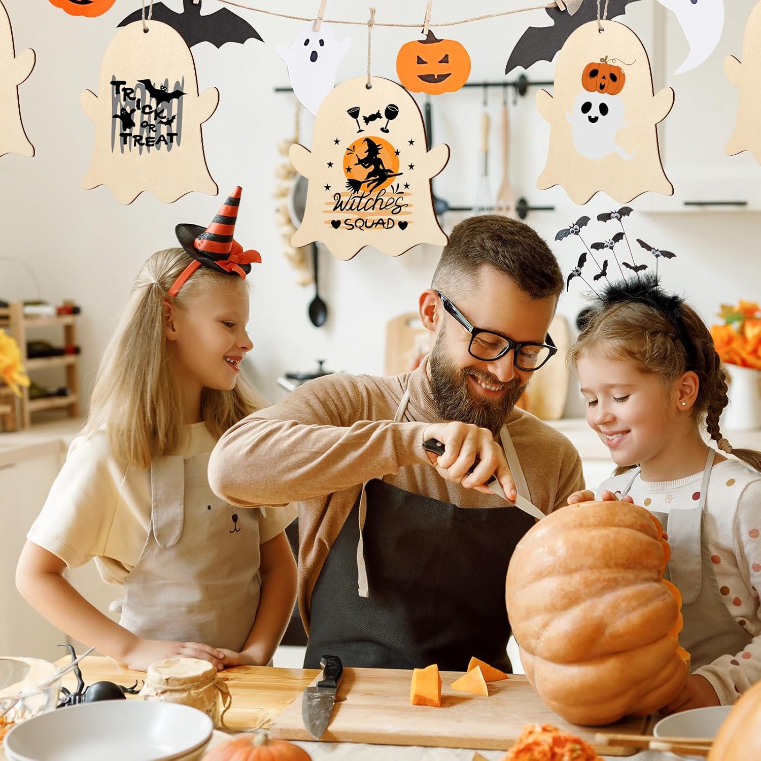 Man and two children carving a pumpkin in a kitchen with Halloween decorations.