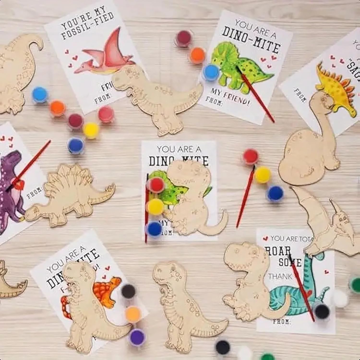Wooden dinosaur shapes with cards and paint supplies on a wooden surface