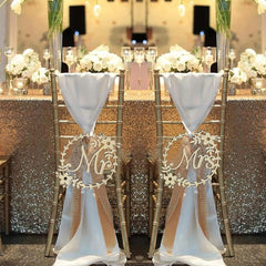 Decorative chair covers with 'Mr' and 'Mrs' signs on a table with floral arrangements.