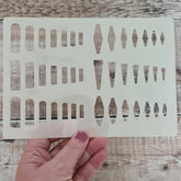 Transparent stenciling template with geometric shapes held by a hand on a wooden surface