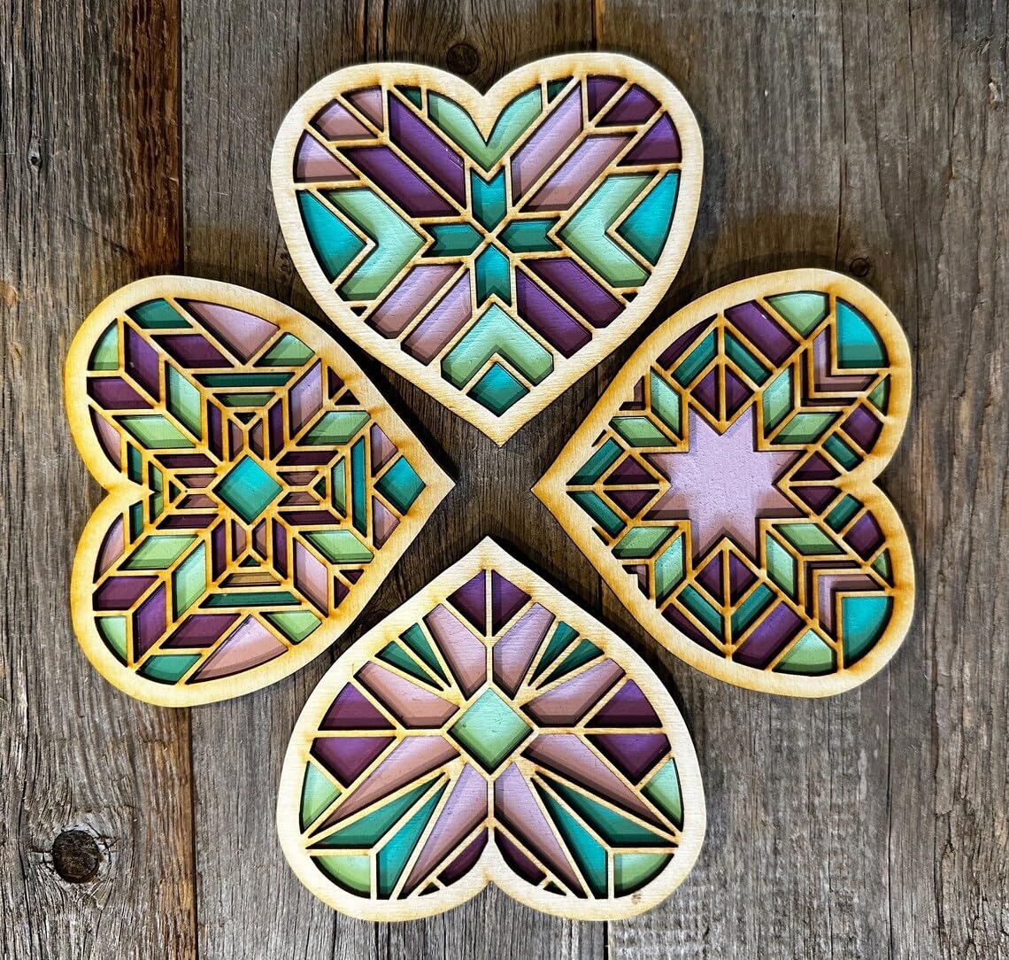 Four geometric heart-shaped coasters with a stained glass design on a wooden surface.