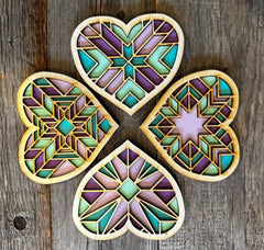 Four geometric heart-shaped coasters with a stained glass design on a wooden surface.
