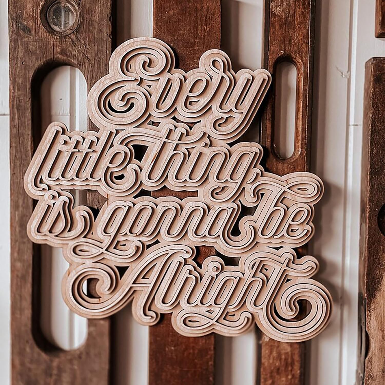 Wooden cutout with 'Every little thing is gonna be alright' text on a wooden background
