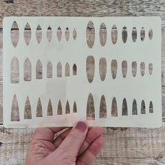 Hand holding a white stenciling template with geometric cutouts on a wooden surface