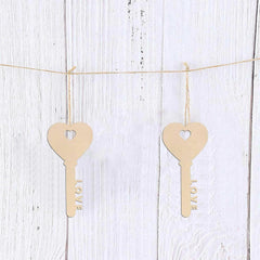 Two wooden key-shaped cutouts with 'LOVE' engraved on them, hanging on a string against a white wooden background.
