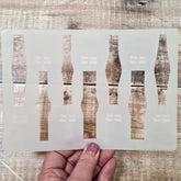 Sheet of bottle-shaped stencils held by a hand on a wooden surface