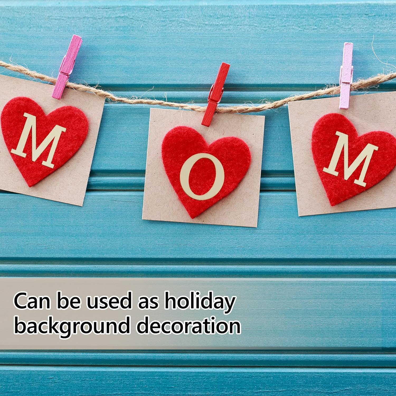Red heart-shaped letters spelling 'MOM' on beige paper, attached to a string with pink and red clothespins against a blue wooden background.