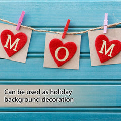 Red heart-shaped letters spelling 'MOM' on beige paper, attached to a string with pink and red clothespins against a blue wooden background.