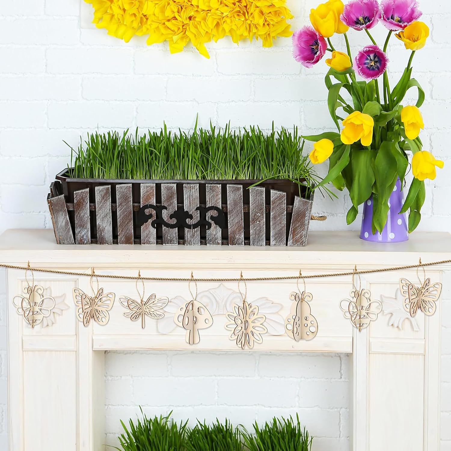 Decorative mantel with grass in a wooden planter and flowers in a vase.