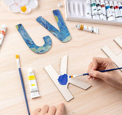 Person painting wooden letters with Van Gogh-inspired designs on a wooden table.