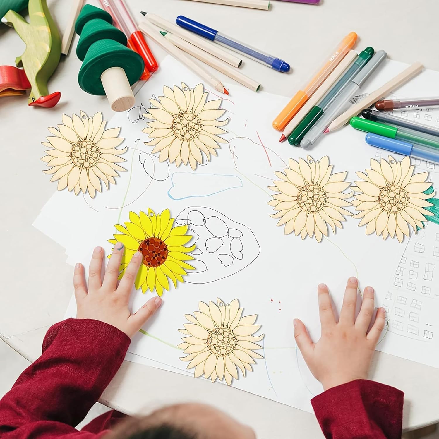 Children's hands coloring sunflowers on a piece of paper with markers and crayons.