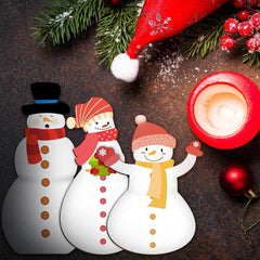 Three snowmen with festive hats and scarves, a lit candle, and Christmas decorations on a dark surface.
