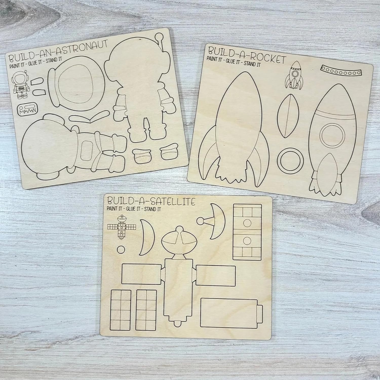 Three wooden templates for building an astronaut, rocket, and satellite on a light wooden surface.