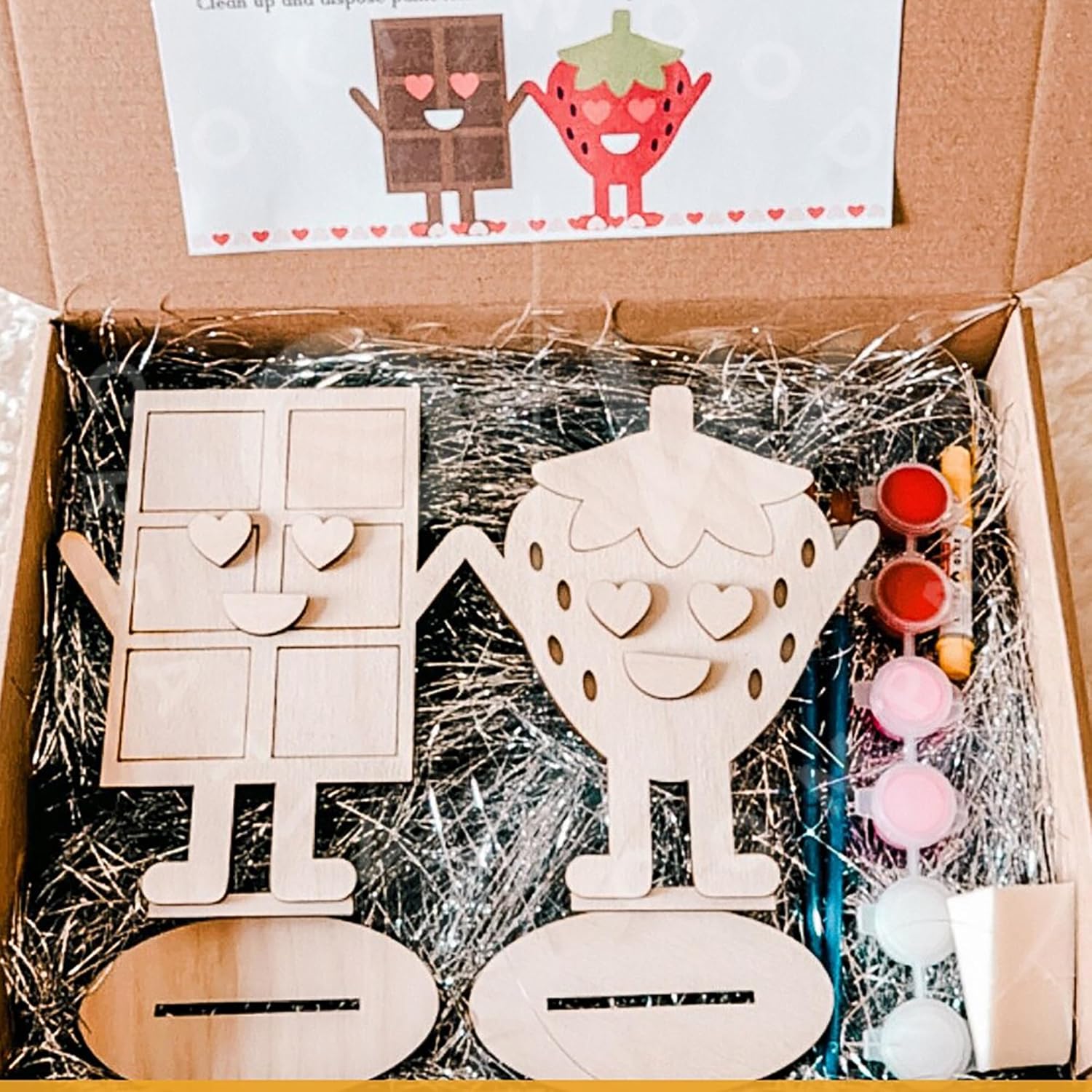 Wooden craft kit with strawberry-shaped figures, paint bottles, and brushes in a cardboard box.