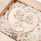 Heart-shaped wooden ornament with 'Bee my Valentine' text on a white shredded paper background