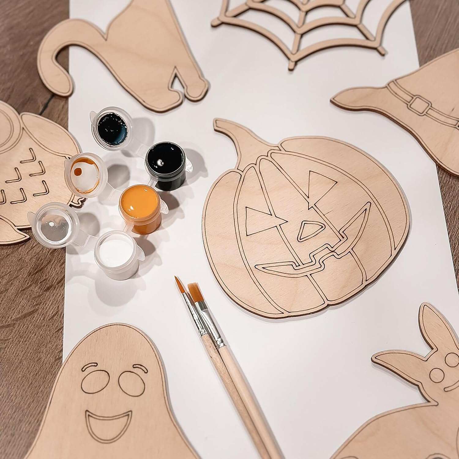 Wooden Halloween cutouts with paint supplies on a white surface