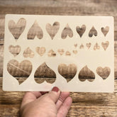 Heart-shaped stencil held by a hand on a wooden surface