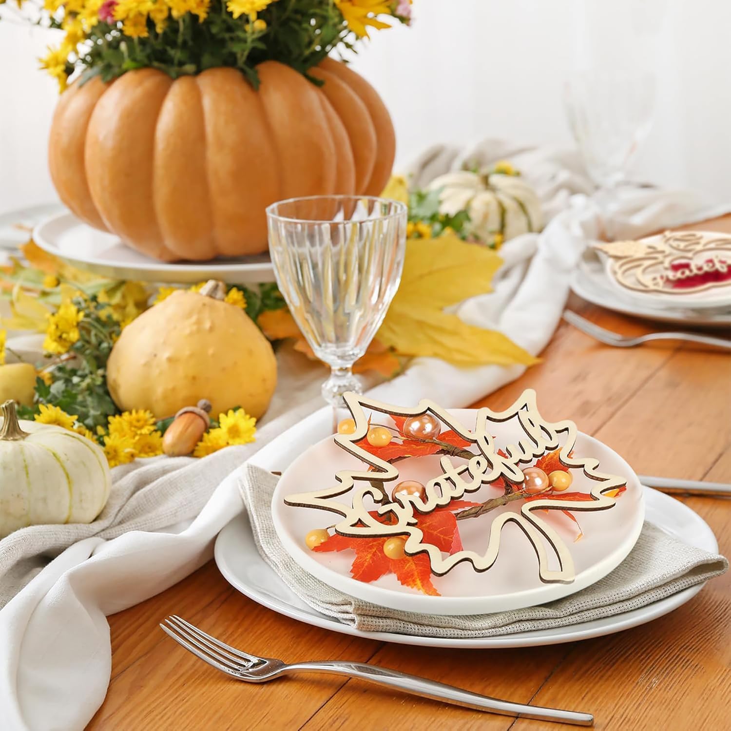 Thanksgiving table setting with pumpkins, leaves, and a decorative leaf on a plate.