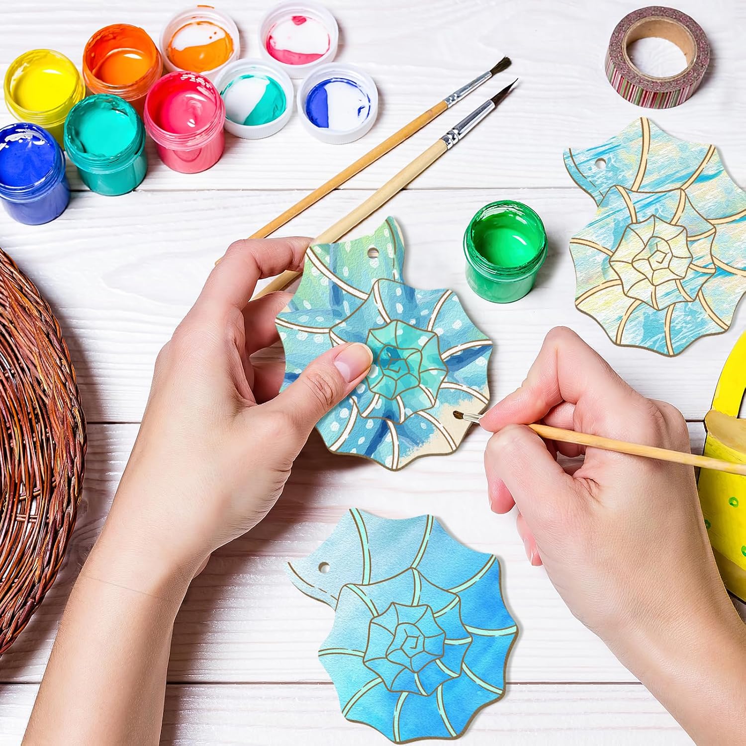 Hands painting decorative wooden pieces with colorful paint and tools on a white surface.