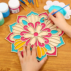 Colorful wooden mandala being painted with a hand holding a paintbrush on a wooden surface.