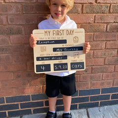 Child holding a sign for their first day of school in front of a brick wall.
