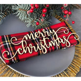 Red plaid fabric with 'Merry Christmas' text on a gray surface with festive decorations.