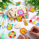 Children's craft materials including wooden shapes, markers, and paint on a table with greenery.