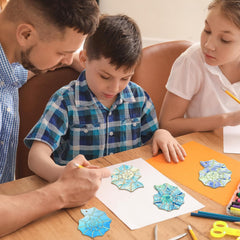 Man and two children working on a craft project at a table with colorful paper cutouts.