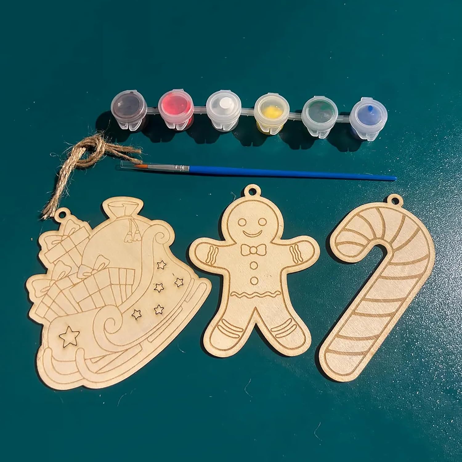 Wooden Christmas ornaments with paint supplies on a teal surface