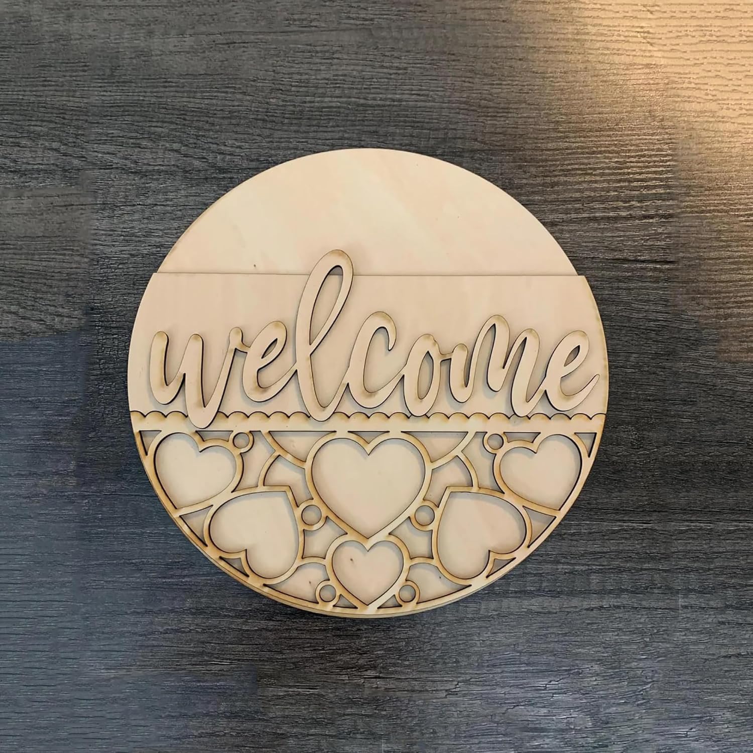 Round wooden sign with 'welcome' and heart designs on a dark wooden surface