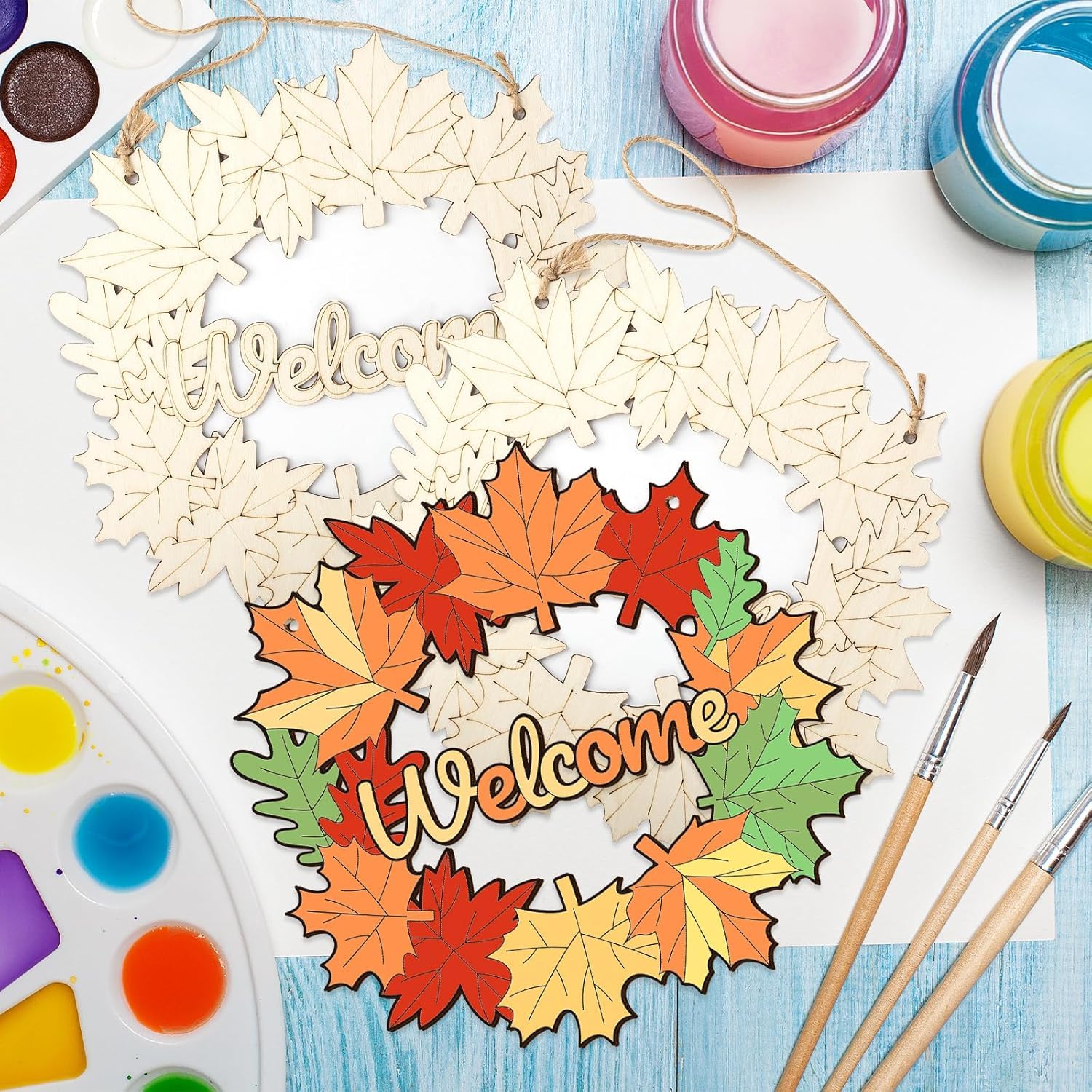 Wooden wreath with 'Welcome' text and colorful leaves on a table with art supplies.
