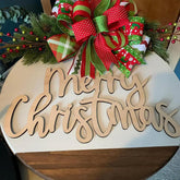 Wooden 'Merry Christmas' sign with a large decorative bow and Christmas decorations on a white surface.