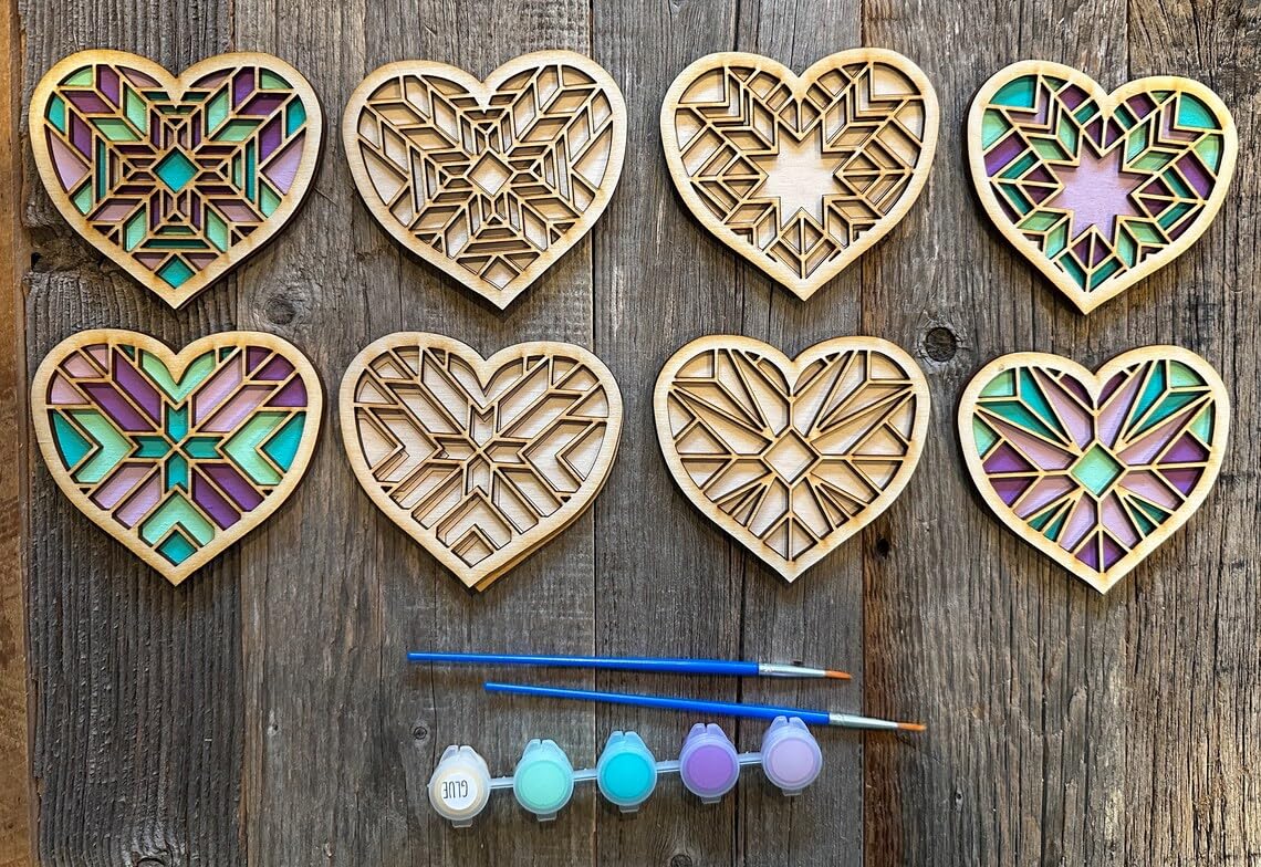 Set of wooden heart-shaped pieces with stained glass patterns and painting supplies on a wooden surface