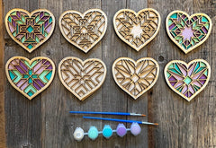 Set of wooden heart-shaped pieces with stained glass patterns and painting supplies on a wooden surface