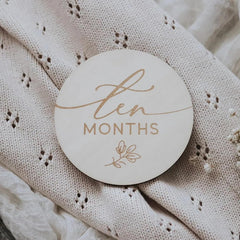 Round wooden coaster with 'ten months' text on a textured fabric background