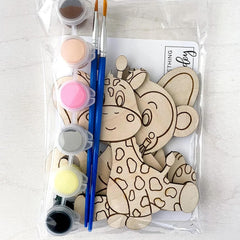 Wooden craft set with paint bottles and brushes, featuring a giraffe design, on a light gray background.